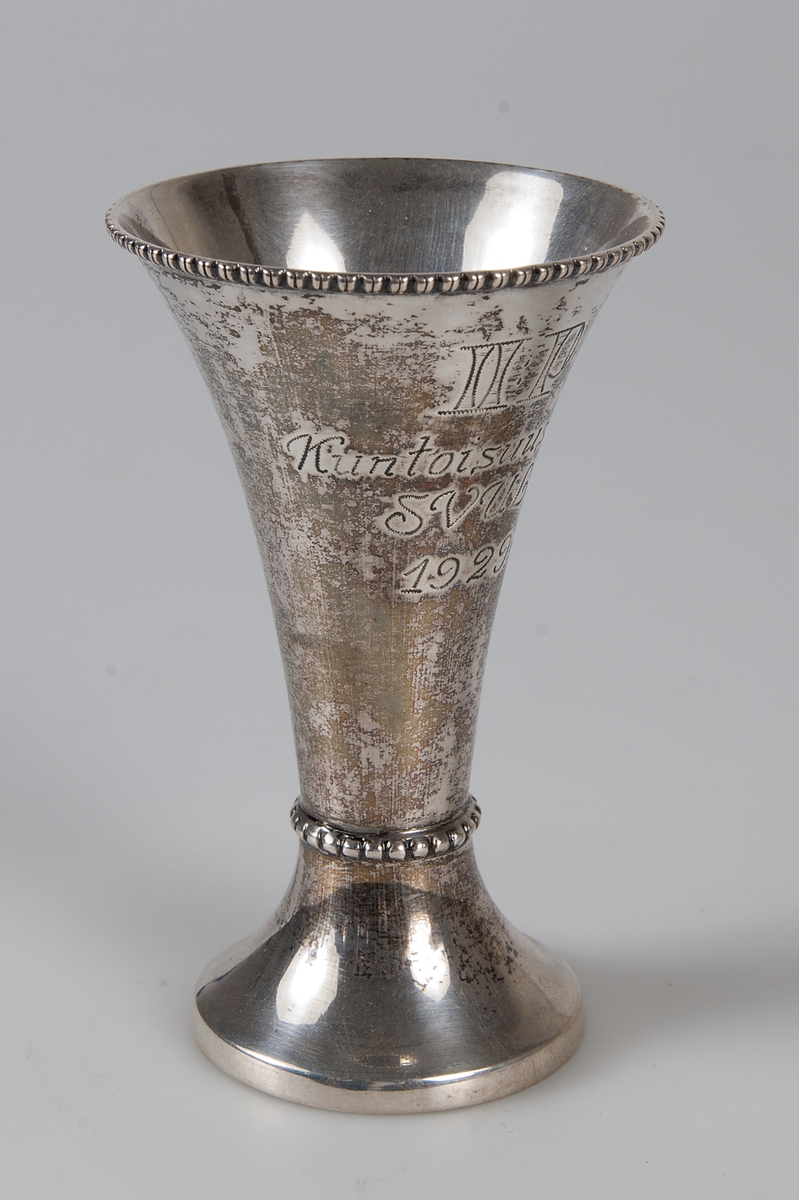 Liten smal silverbägare med dekor runt mynning och vid fotens början. Ingraverat: II:P, Kuntoi, suus, sajo, SVUL, 1929.