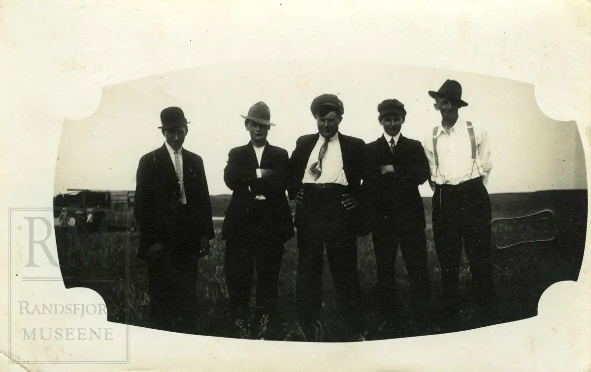 Fem menn oppstilt på rekke, med dress og hodeplagg