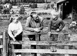 Alf Prøysen med 2 barn ved grinda foran Prøysenstua, Ringsak