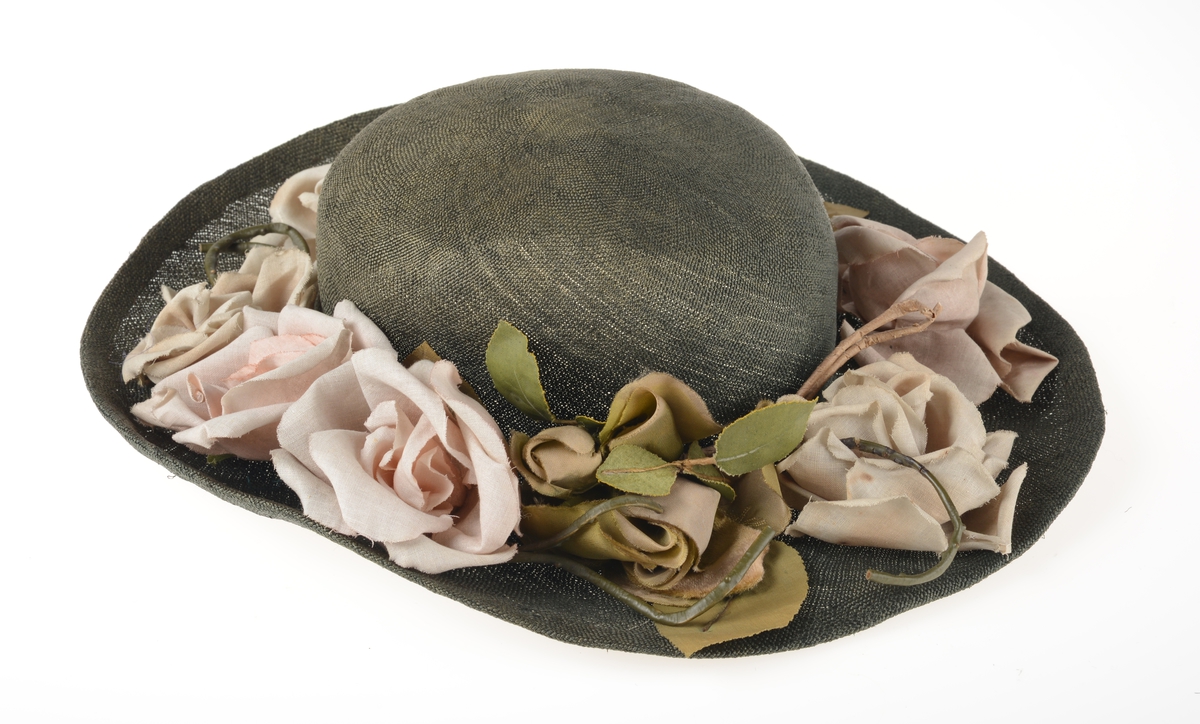 Hatten har rund pull med vid brem som er pyntet med stoffroser og blader.  Det er lagt inn en metallstreng ytterst i bremmen.