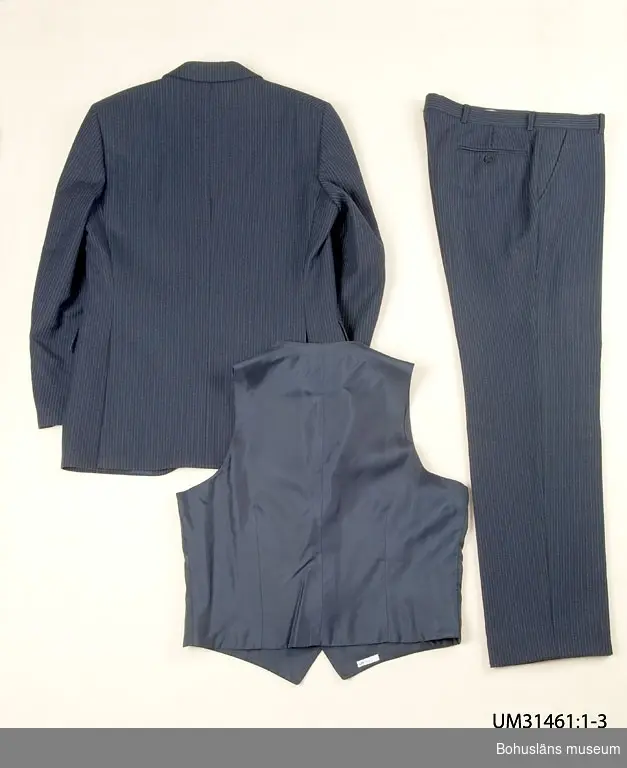 Mörkblå kostymbyxa (UM31461:1) sammanhörande med kostymkavaj (UM31461:1) och kostymväst (UM31461:3).
410 Mått/Vikt  Benlängd 79 cm  Benvidd 21 cm

Kostymbyxa i mörklblå ull med smala kritstreck. Ofodrade. Linning med hällor för bälte, knäpp framtill med slejf. Gylf med dragkedja, Två snedställda sidfickor, en infälld bakficka med dekorknapp. Fickor av vitt bomullstyg. 
På insidan firmaetikett med texten:
"TIGER OF SWEDEN
STORL.
SIZE.
GRÖSSE  B 48.
451 26 UDDEVALLA
På baksidan uppgifter om kvalitet och tvättråd.