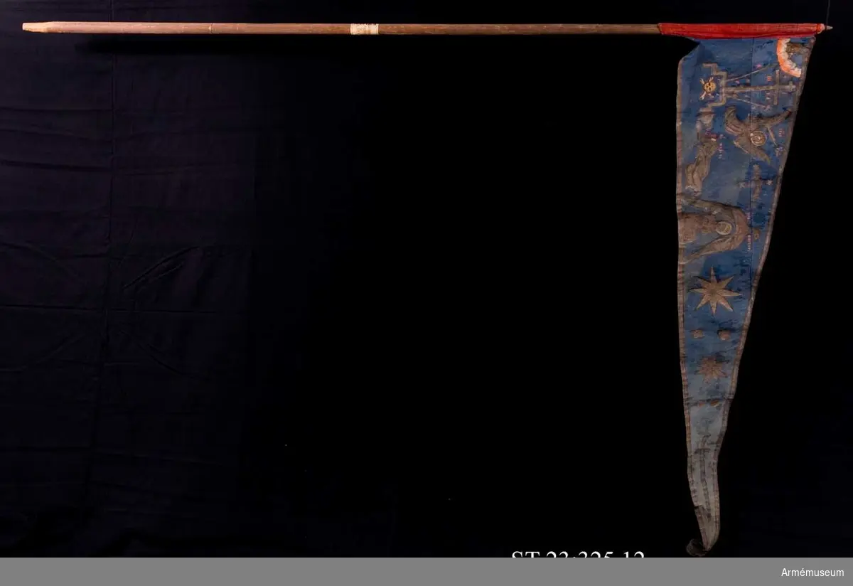 Duk av blå kinesisk sidendamast med målad dekor. Motivet föreställer den romerske kejsaren Konstantins vision av ett kors i skyn kvällen innan slaget vid Pons Mulvius år 312 e Kr mot Maxentius. En ärkeängel med svärd i handen (Gabriel?) svävar över den halshuggne Maxentius. Denna händelse ses som förklaring till att kristna kors började användas på militära fanor. Närmast stångsidan är också ett Golgatakors avbildat. Över detta syns ett moln där Kristus är avbildad. 
Strumpa av rött linne.