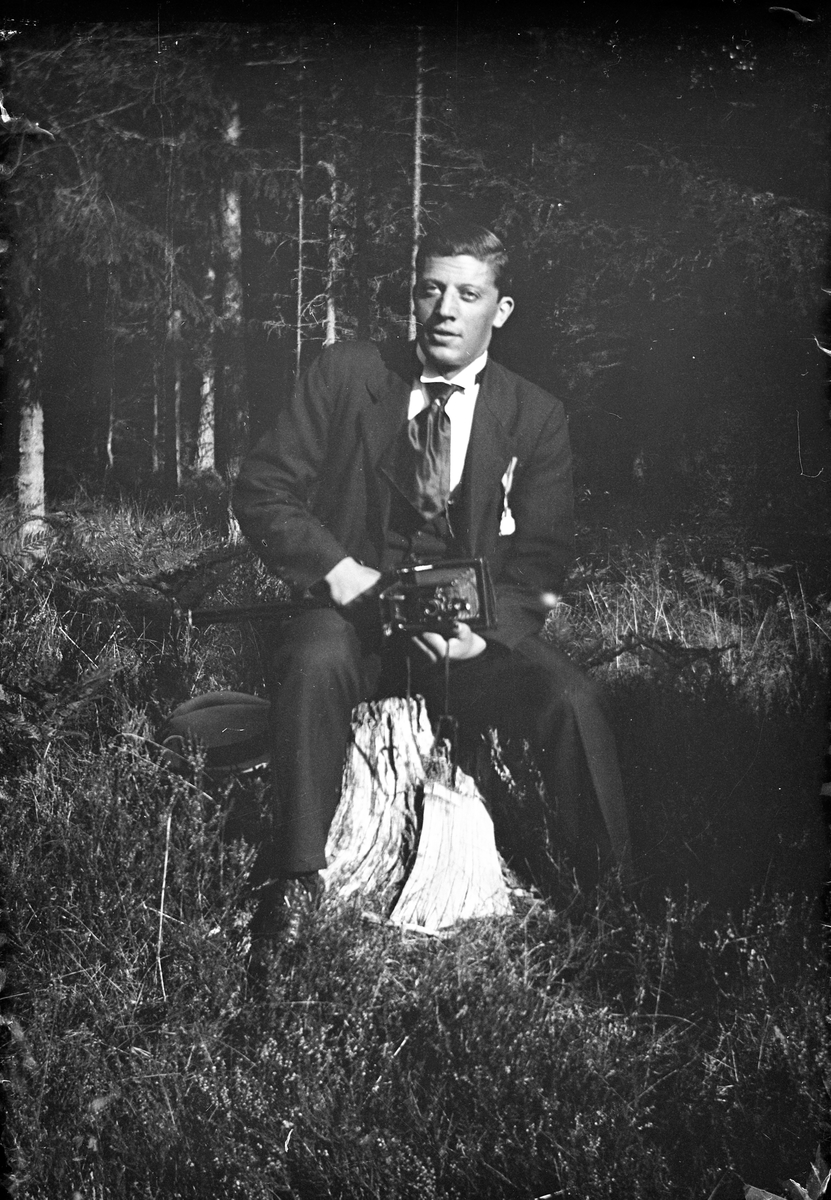 En man med kamera i knät sitter på en stubbe i skogen vid Lungkliniken i Eksjö.