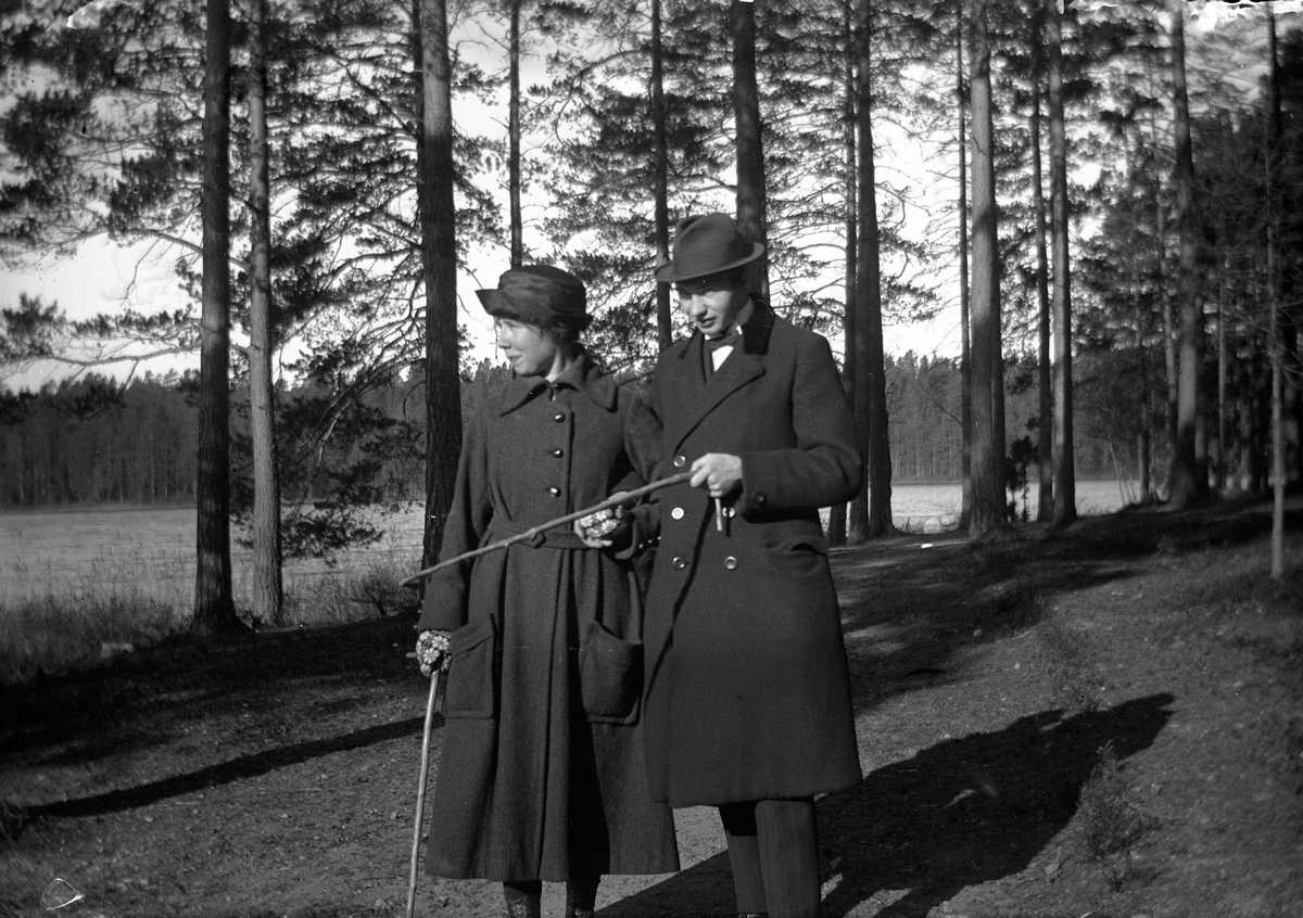 En man och en kvinna går arm i arm, båda med käppar, vid sjön i barrskogen vid Lungkliniken i Eksjö.