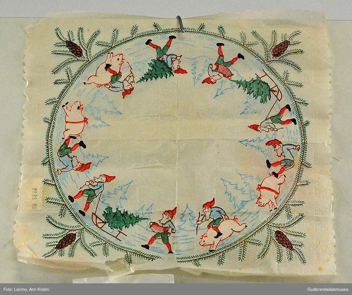 Papirserviett med "frynsete" kant, julemotiv av nisse på gris, kongle på grein, nisse bærer/drar juletre på slede og på ryggen, motiv i sirkel.