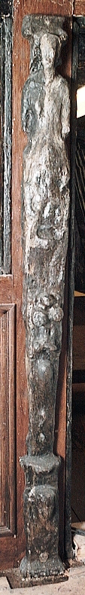 Skulpterad pilaster utformad som en karyatid med långt hår, troligtvis placerad under ett joniskt kapitäl.
Huvudet och kroppen är frontalvända. Höger arm är sträckt utefter sidan. Vänster arm är böjd och i handen håller figuren ett okänt föremål.
Pilasterskaftet är upptill prytt med en maskaron med bred, öppen mun och nedtill med en tung fruktfeston. Det nedåt avsmalnande pilasterskaftet avgränsas från piedestalen av en enkel vulst eller list med uppdragna kanter. Piedestalen är hög och jämnbred samt prydd med ett litet huvud och avslutas nedtill med en förtjockad bas. Skulpturens baksida är slät.
Skulpturen är mycket sliten.

Text in English: Sculpted pilaster with Caryatid with long hair under what is possibly an Ionic capital.
The figure''s head and body are turned to the front. The right arm is streched along the side, the left arm is bent and the hand holds an unknown object.
The shaft of the pilaster is decorated above with a mask with broad, open mouth, and below with a heavy festoon of fruit. The shaft tapers downwards and is divided from its pedestal by a simple torus or batten with drawn-up edges. The pedestal is high and even in width. It is decorated with a small head and terminates at the bottom in a thickened base. The back is smooth.
The sculpture is very much worn.