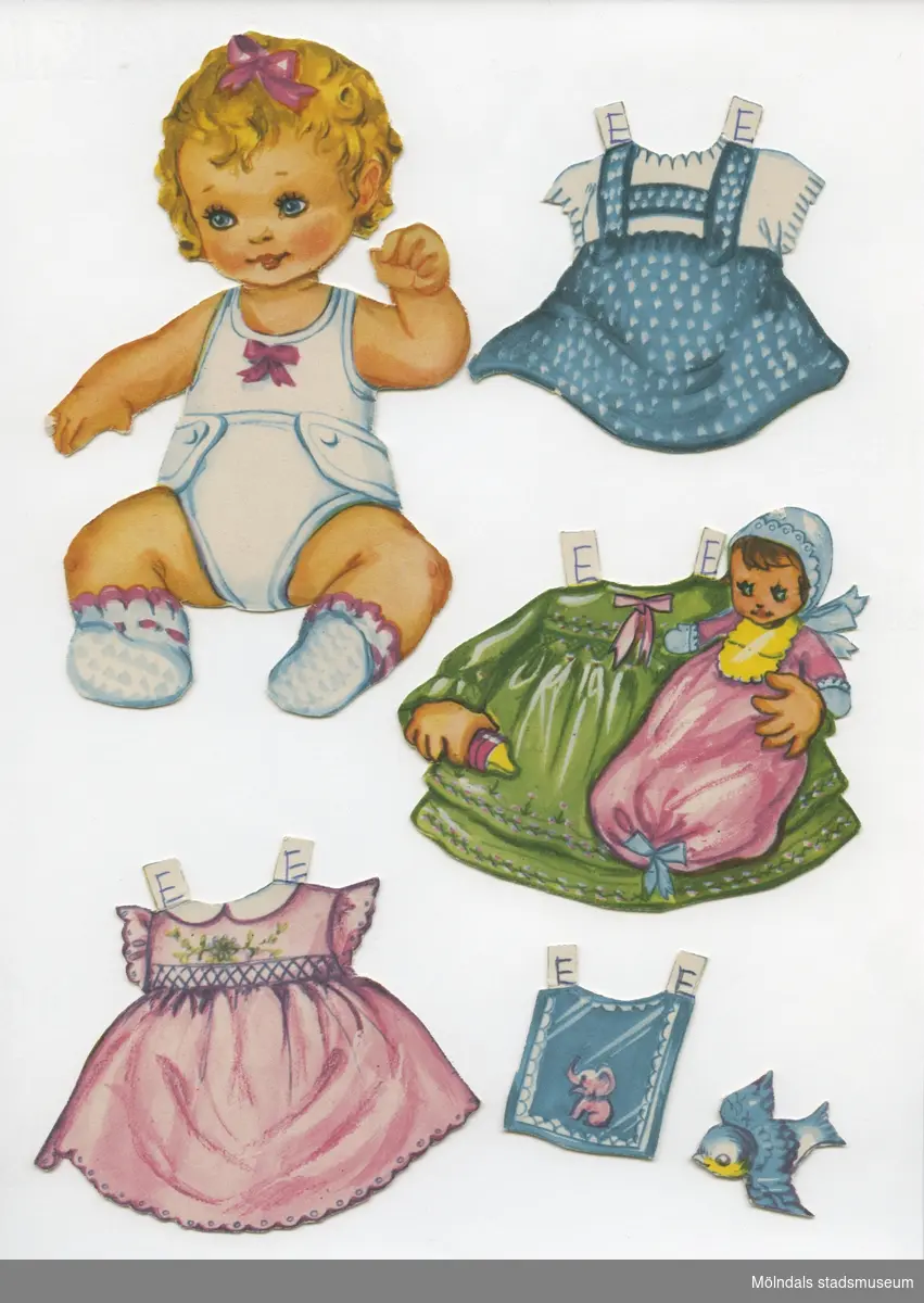Klippdocka med kläder och tillbehör från 1950-talet. Docka och kläder märkta "Eva" - dockans namn.Dockan, av papp, föreställer en baby, med blont hår, iklädd linne, tygblöja och sockar. Garderoben består av tre  klänningar, pyjamas och ett vinterplagg med kapuschong. Dockan har dessutom tillbehör som hakklapp och leksaker (bollar, klossar, skallror, mm). Vissa föremål är märkta både "Eva" och "Dan" (MM 04588).