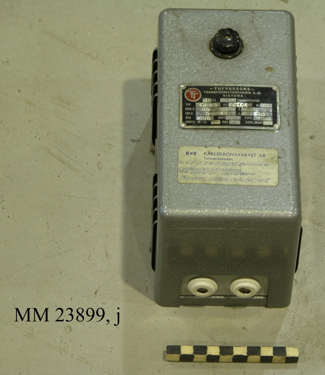 Silvergrå laddningsriktare typ EA-358035-S till Marinens riktade radiofyr. Märkt "TT" på båda sidorna. Metallplatta framtill. Klisterlapp framtill med texten: "Karlskronavarvet AB, Televerkstaden". Marinens riktade radiofyr består totalt av flera olika delar: sändare (antenn), filterstativ, sändarram, startbox, rambox, teckengivare, laddningslikritare, kontrollmottagare, likritare mm. Alltsammans drevs av ett portabelt elverk.