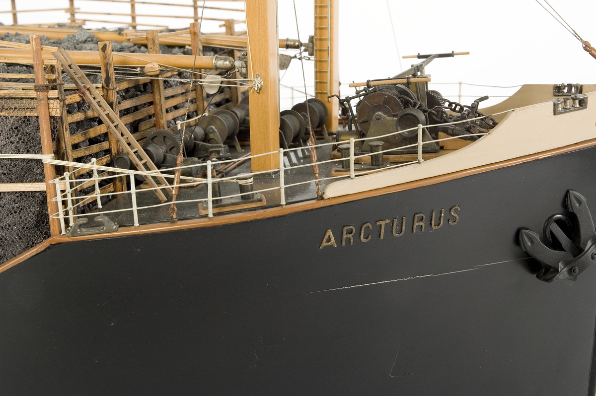 Fartygsmodell, hel i block av trä och metall, lastångfartyget "Arcturus" av Torö, förande sommardäckslast av koks, svartmålat skrov med rak stäv, röd bottten, vita däckshus midskepps och akter, svart skorsten med 3 vita band och en j cirkel, 4 par fyrsida bomposter, midskepps 4 vita livbåtar (en eka) i dävertar.