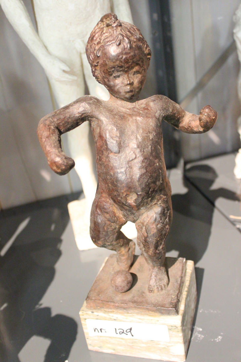 Skulptur i bronse av et barn på sokkel av marmor. Tittel: "GUTT MED BALL". Se også nr.107, nr.108, nr.127 og nr.128.