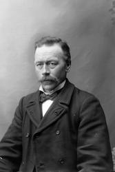 Studioportrett i halvfigur av en mann med bart.