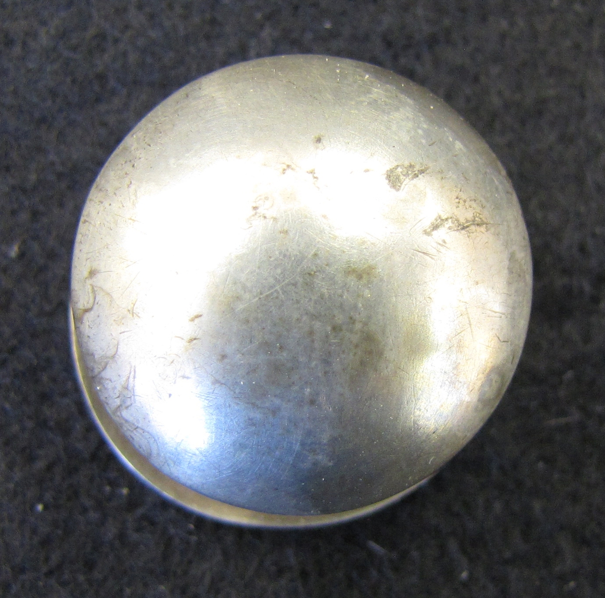 Allmogeknapp med halvrunt, helt slätt, huvud. Knappen är fästad i en välvd rund bottenplatta och fungerar likt en manschettknapp.

Stämplad AS, men då ett stort antal silversmeder under 17-1800-talet stämplade med dessa initialer har någon tillverkare till denna knapp ej med säkerhet kunnat fastställas.