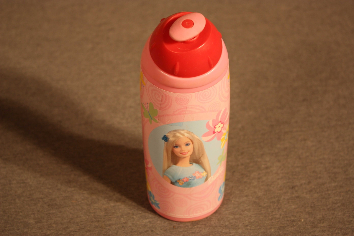 Plastflaske  med skrukorkog drikketopp. Flaska er forma til handgrep. Pålimt etikett med brystbilete av ei Barbiedokke i midten. Skrive Synne E. med tusj under botnen.