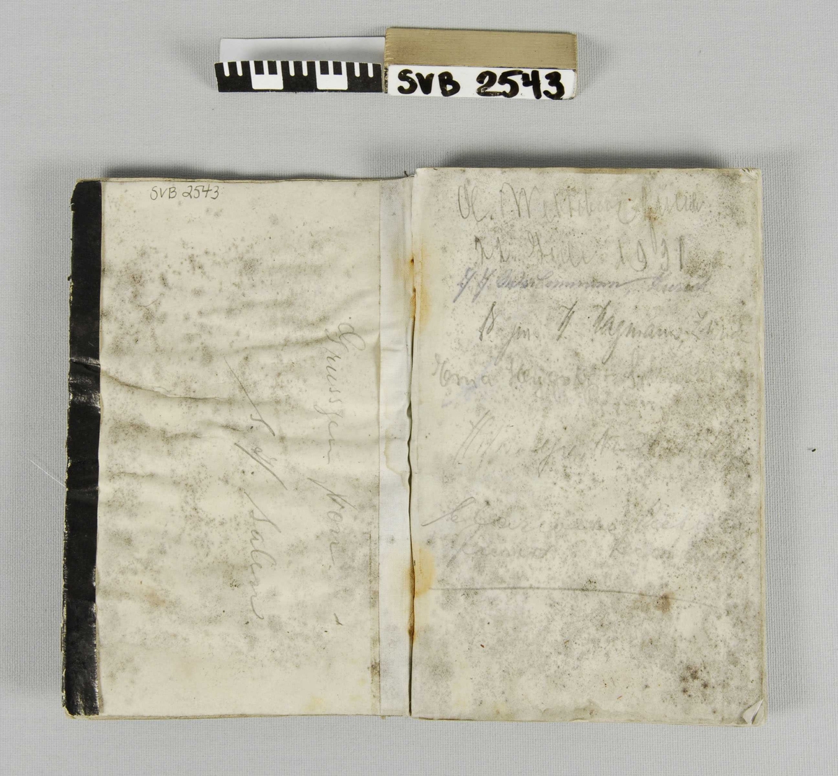 Notatbok med omslag i sort papir, sort tekstilrygg. Hvitt etikett med påskrift i blekk.