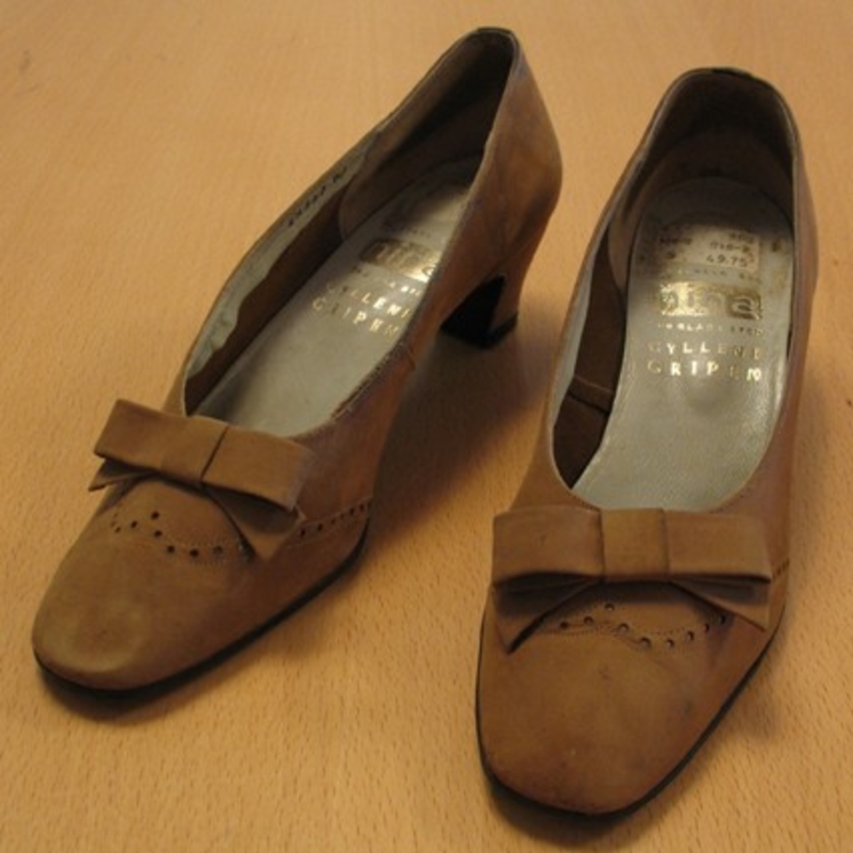 Ett par skor.

''Fotvänlig sko. Nina för glada steg. Gyllene Gripen''.

Damsko med halvhög klack, pumpsmodell med rosett.