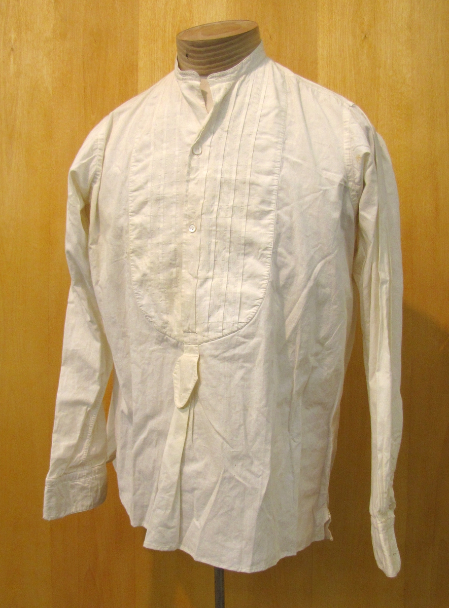 Herrskjorta, så kallad frackskjorta i bommull.

Skjortan är inköpt av brukaren Hugo Tibblin i ekiperingsaffären Arvid Bergström som var en fin och välrenomerad ekiperingsaffär i Vänersborg. Affären låg i hörnet Edsgatan-Kungsgatan. 

Hugo Tibblin inhandlade skjortan då han gjorde sin stora resa till USA och fanns med i kofferten som han hade med på resan.

Vänersborgaren Hugo Tibblin (1897-1964) blev tidigt föräldralös och kom att växa upp i ingifte morbrodern, konditor, Edvard Nordfeldts hem. Inspirerad av morbrodern kom Hugo att utbilda sig inom bagar- och konditoryrket. Med föräldraarv på fickan gav han sig år 1926 av på en resa till USA med sina tre vänner Ernst Sjöö, Ernst Petré och Westerlund. I Seattle på den amerikanska västkusten bodde Hugos faster Evelina med familj. Resan gick från Göteborg med MS Drottningholm till New York och sedan vidaremed tåg till Seattle. Under tiden i USA prövade Hugo även på bagaryrket underen tid vid Hansen Bakery i Seattle. Hemresan gick längs västkusten, via Panamakanalen och Cuba, till New York. Där blev det byte av båt hem till Sverige. Väl hemma i Vänersborg kom Hugo Tibblin att fortsätta sin karriär som konditor vid Nordfeldts och Frisks konditorier. Han visade även en stor konstnärlig talang och målade bl.a. dekorer för Vänersborgsrevyn under många år.