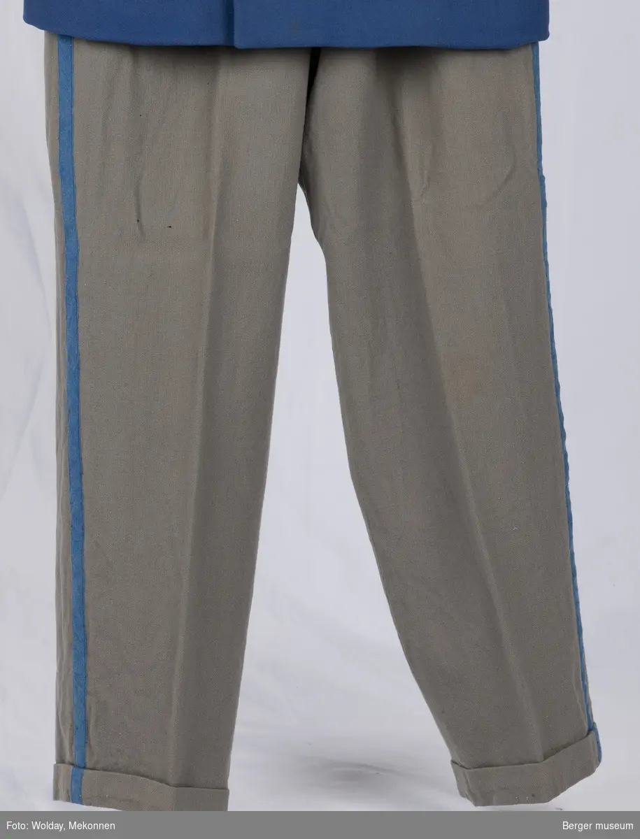 Buksene er grå med en kornblå stripe nedover fra linningen fra begge sider. Buksene har sidelommer, baklomme og en liten lomme foran. Linningen er foret.