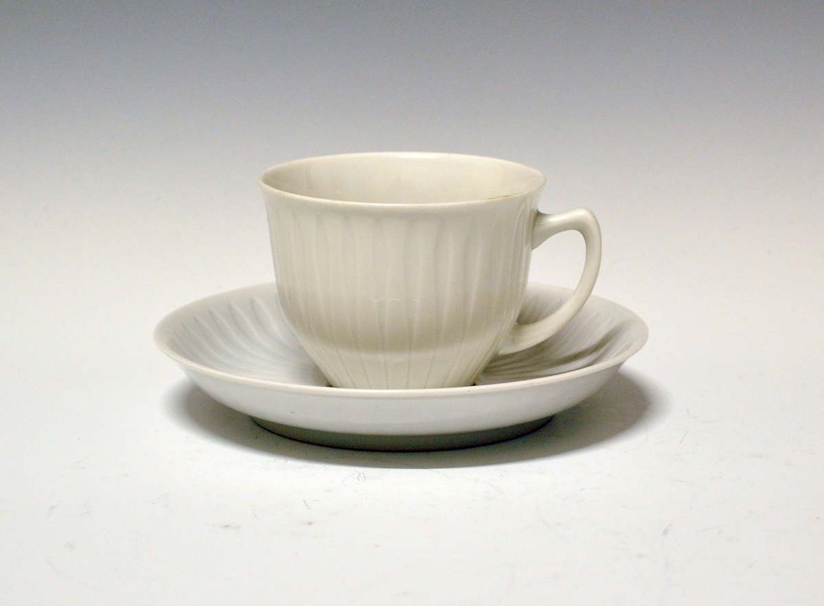 Kaffeskål av porselen. Hvit med vertikale riller som er brede ytterst og smalner innover.
Modell: Spire, tegnet av Konrad Galaaen. I produksjon fra 1952.