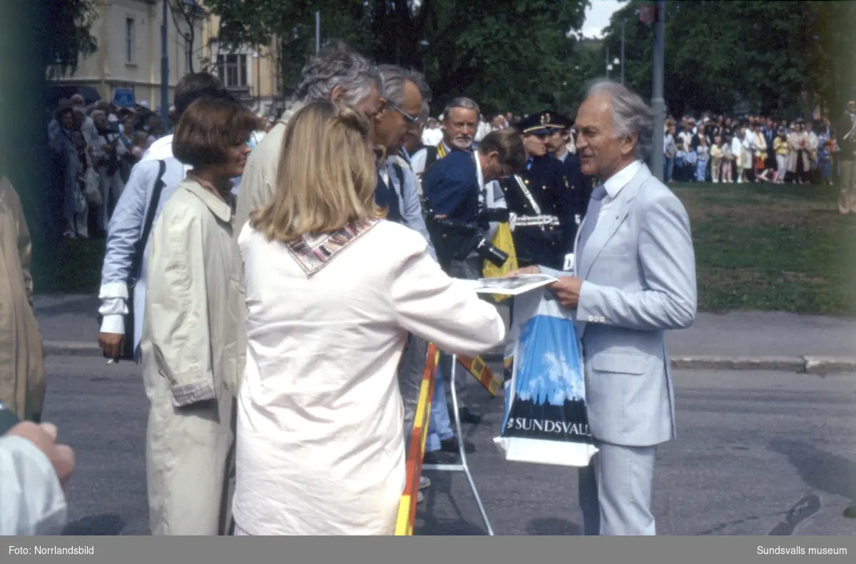 Kungligt besök i Sundsvall av kung Carl XVI Gustaf och drottning Silvia. Stort pådrag med körsång, folksamling, poliser och pressfotografer.