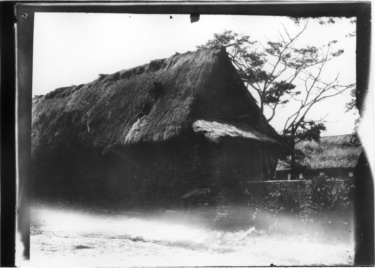 'Diverse fotografier från bl.a. dåvarande Nordrhodesia, nu Zambia, tagna av Konsul Magnus Leijer. ::  :: Tegebyggnad med mur och halmtak.'