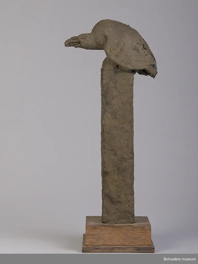 Skiss till större verk. Rovfågel skulpterad i plastisk massa placerade på en hög sockel av av furu, på tre sidor klädd med massa. Allt placerat på en lägre sockel av ek.
Personuppgifter kring konstnären se UM026282