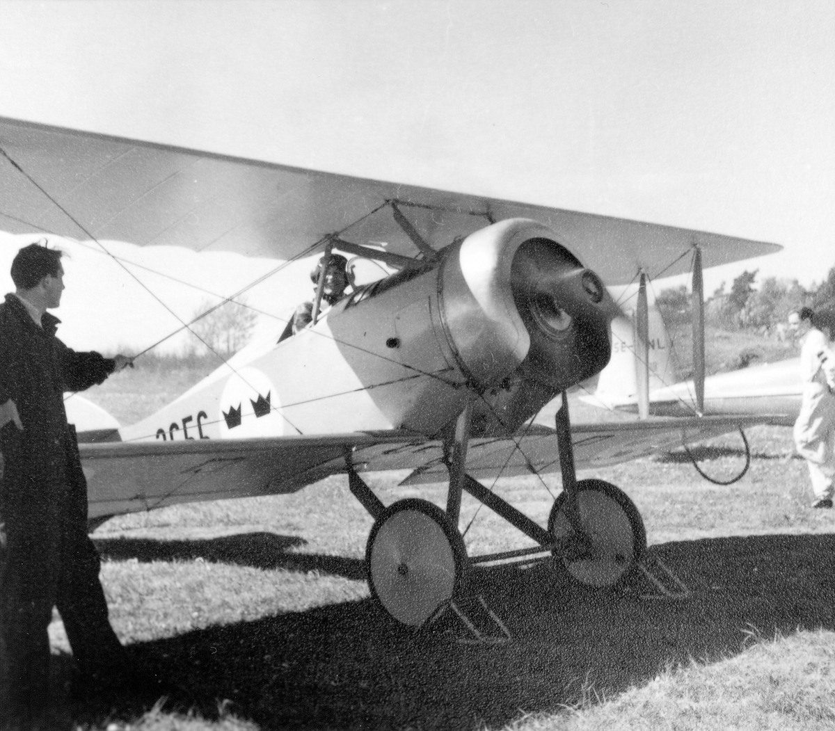 Flygplan Tummeliten, Ö 1 nummer 3656 med förare motorkörs på flygfält. En mekaniker står vid sidan o
