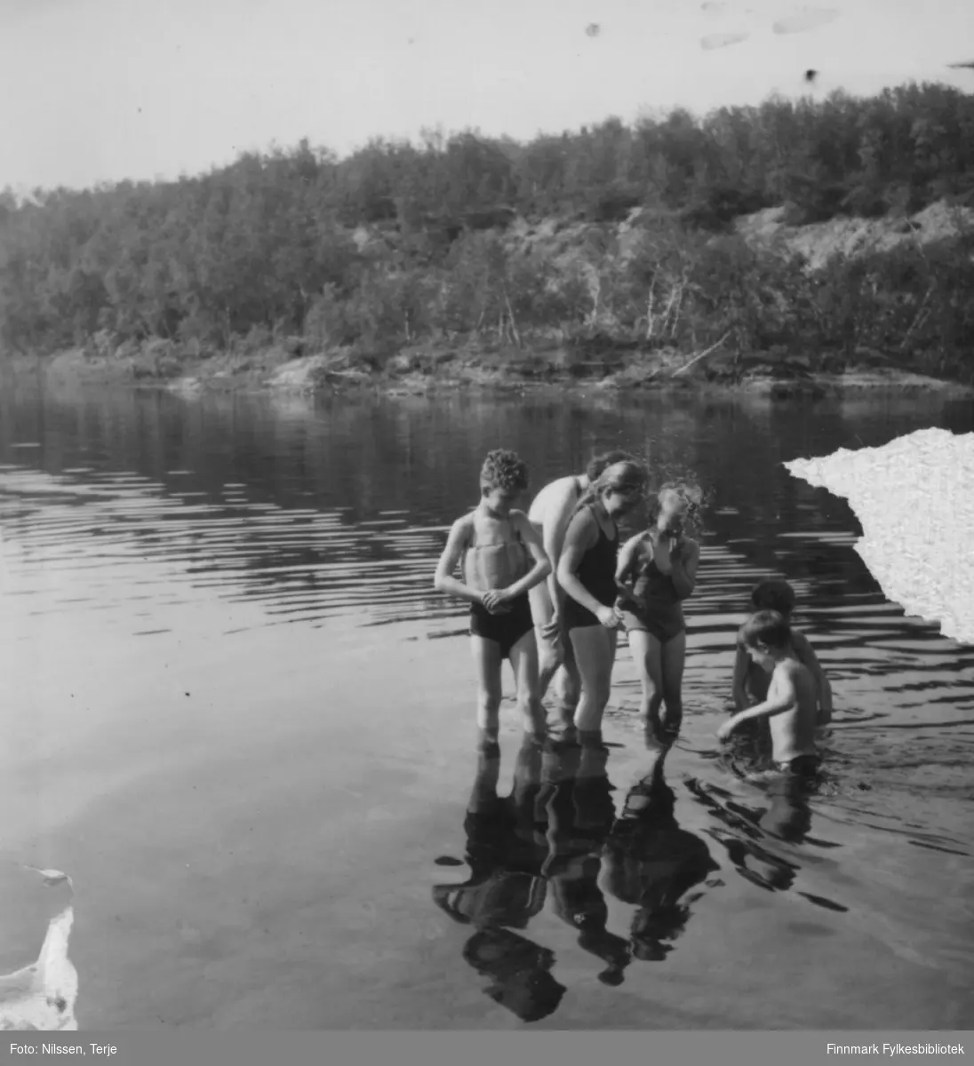 Badeliv sommeren 1957 i Øvre Neiden ved fjellstua. Personene på bildet er fra venstre Arild Nilssen (med svømmebelte) og Mari-Ann Nilssen. Bak Arild og Mari-Ann er hennes mor, Grethe Nilssen. Jenta til høyre er Turid Drannem (Karikoski). De fire står på en stein i elva. Gutten som går i vannet er Oddvar Arvola, og bak ham Egil Nilssen. 