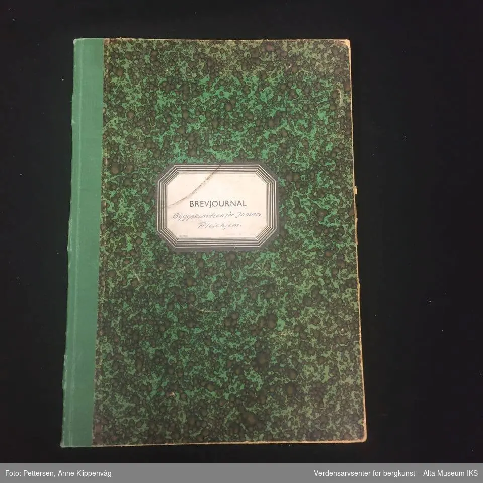 Rektangulær notatbok, innbundet med harde permer. Grønn og sortmønstret på forsiden og baksiden.
