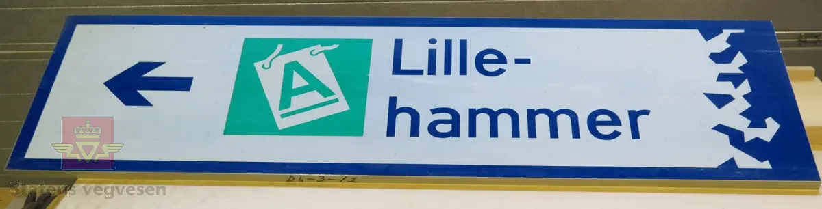 Rektangulært skilt av aluminium. Har symbol for kjøreretning samt teksten "A  Lille-hammer". Blått, grønt og hvitt, med grå bakside.
