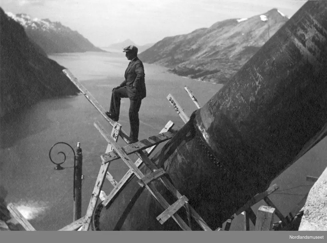 Utsyn mot Glomfjorden. Rørgata i forgrunnen. Mann (Bernt Lund) poserer på stillas på rørgata.
