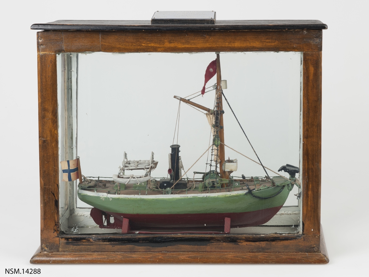 Enkel helmodell (sjømannsmodell) av hvalbåt i monter. Grønt skrog, mast, skorstein, 2 lettbåter, hvalkanon.