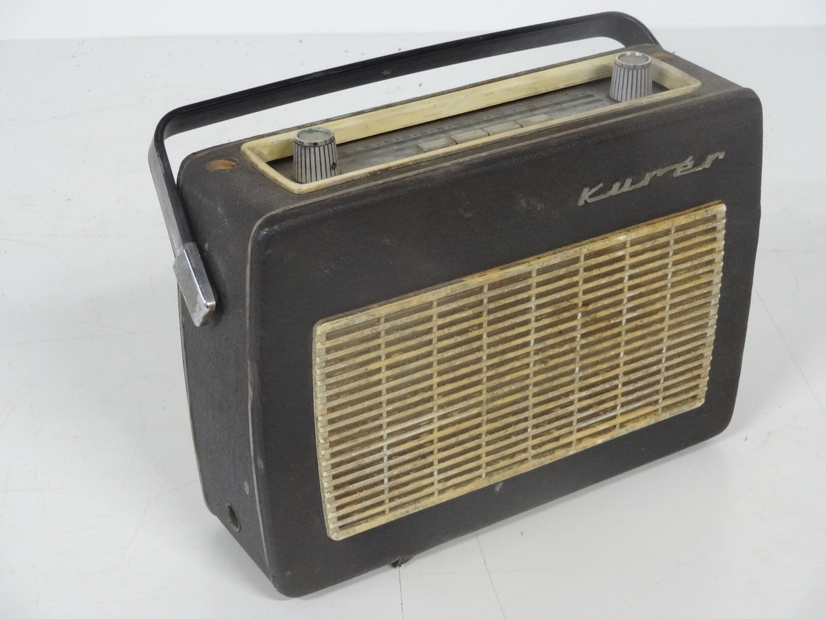 Transistorradioapparat fra Radionette av type Kurér med tilleggsbetegnelsen "Marine deluxe". 

Radioen har merker på undersiden som forteller at den kostet 590 kr og hade en stempelavgift på 47,50 kr. Apparatet fungerer ikke.  Det er og mulig å koble til båndspiller / grammofon.

Batteri er borte.