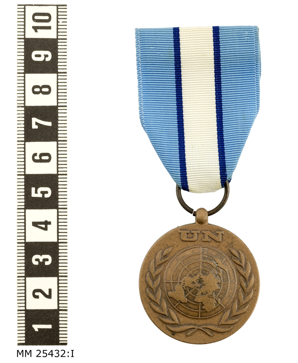 Cirkelrund medalj i brons. På framsidan FN-emblem i releif med världskarta omgiven av lagerkrans under text "UN".. På baksidan text "IN THE SERVICE OF PEACE": Överst på medaljen en knoppliknande hållare med hål i varigenom on kopparring löper. Kopparringen fäst i ett band av sidenrips. Bandet har två ljusblå fält lägst ut på kanterna och ett vitt fält i mitten separerade av mörkblå streck. Längst upp på bandet sutter nål att fästa i uniformen.