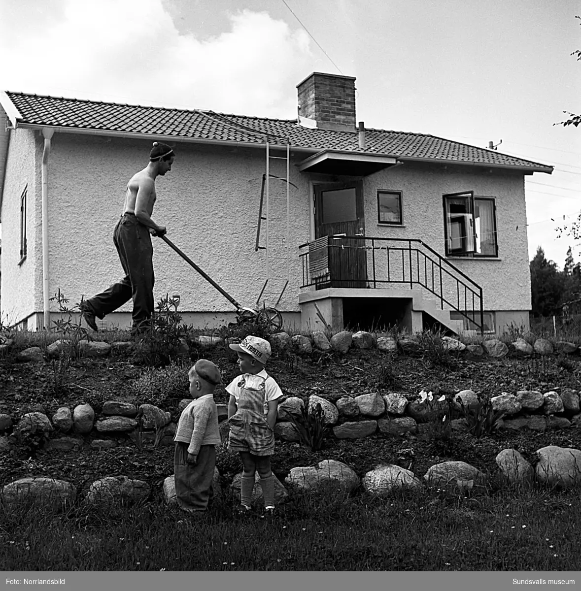 Nytt bostadsområde på Östermalm, Rebetskygatan. Trädgårdsarbetande män och två små pojkar som luktar på blommor.