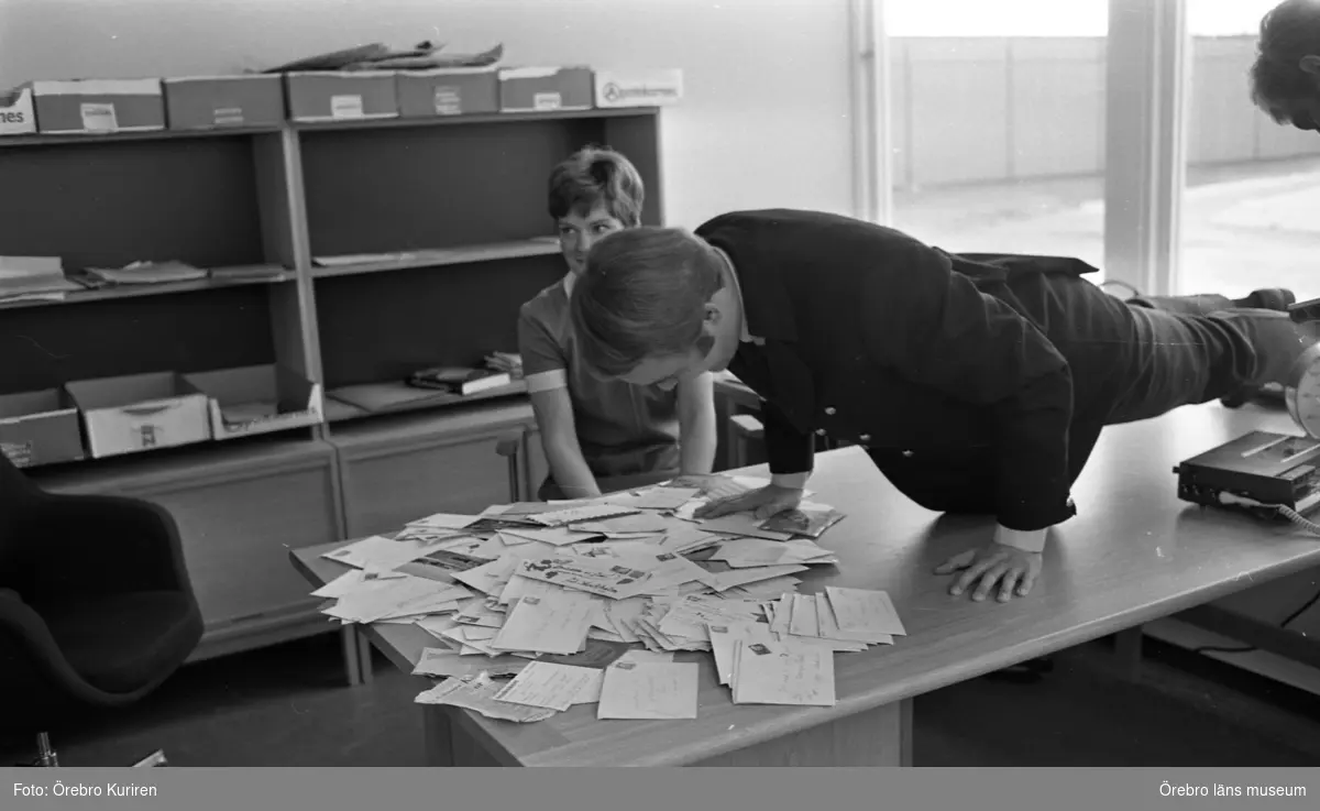 Bryggaren 2 - 1 februari 1969

Sten Nilsson gör armhävningar på ett skrivbord. På  skrivbordet ligger det mycket brev. En kvinna i klänning sitter på en stol vid skrivbordet. Bakom henne ser man skåp med hylla.