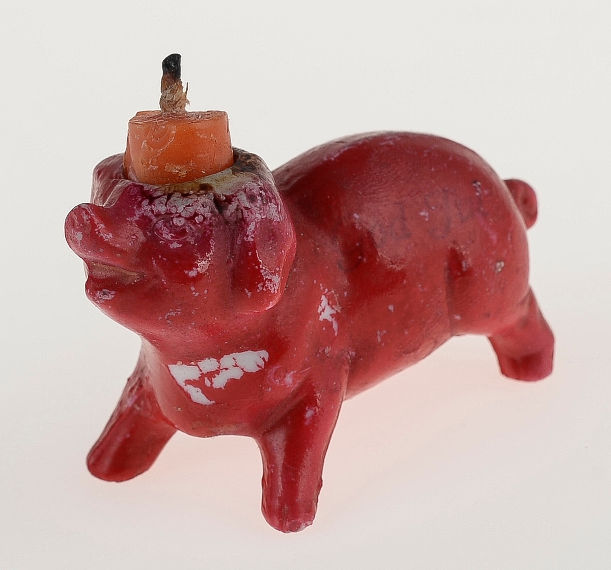 En liten lysestake som er en rød julegris. Lyssokkelen er i grisens hode. Det står igjen en oransje lysestump.