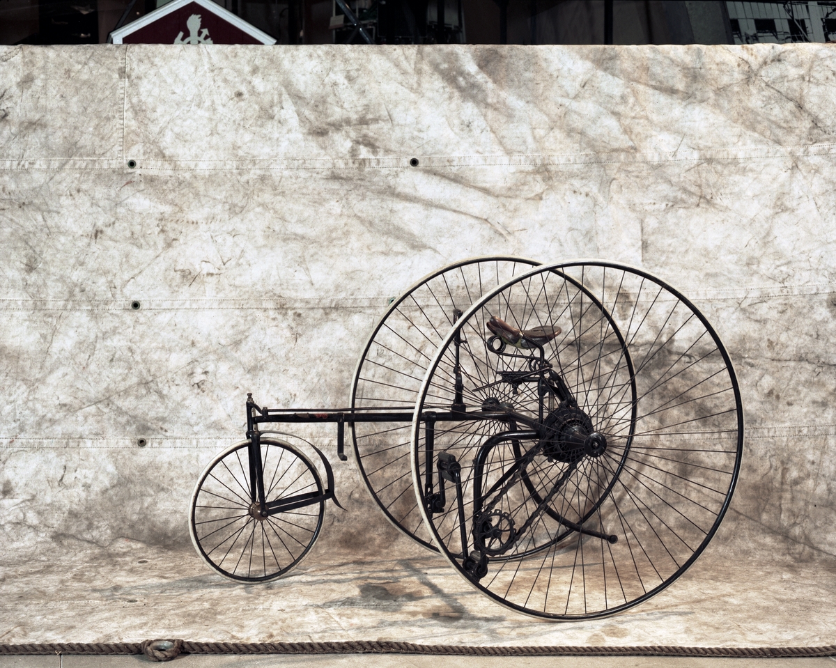 Trehjulig cykel. Styrning med högerhandshandtag som påverkar kugghjul-kuggstång. Bromshandtag för vänsterhand. Kedjedrift. Två stora bakhjul, ett litet framhjul och "damsadel", vilken är mycket trasig. Massiva däck. Märkning: The Royal Mail Tricycle, på sköld av mässing. Röd dekal: The Royal Machine Manufacturing Co Ltd, Birmingham.