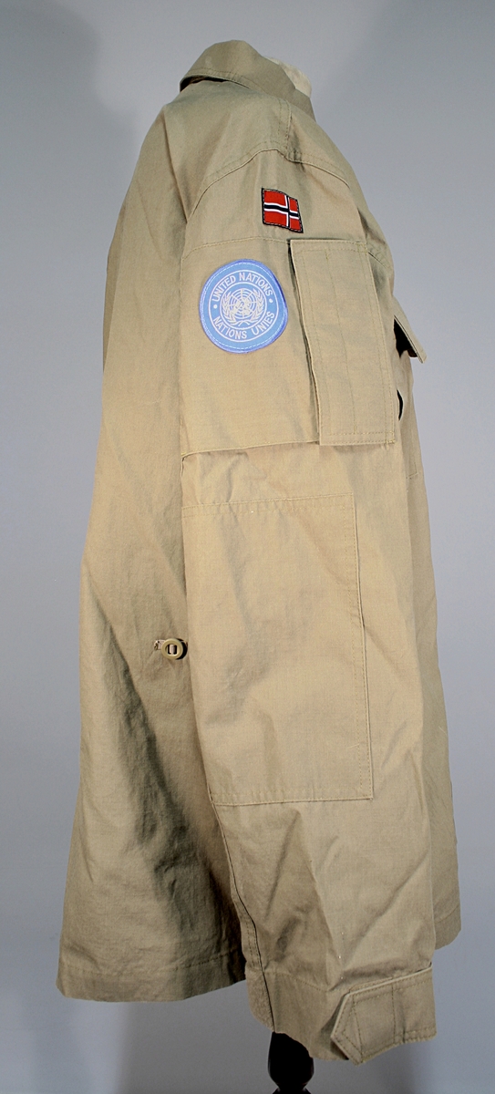 Khakifarget jakke med politimerking etter 1995-reglementet. Norsk flagg og FN-merket på høyre skulder. Distinksjon for politioverbetjent festet på brystet. To brystlommer og en lomme på hvert erme som lukkes med borrelås.