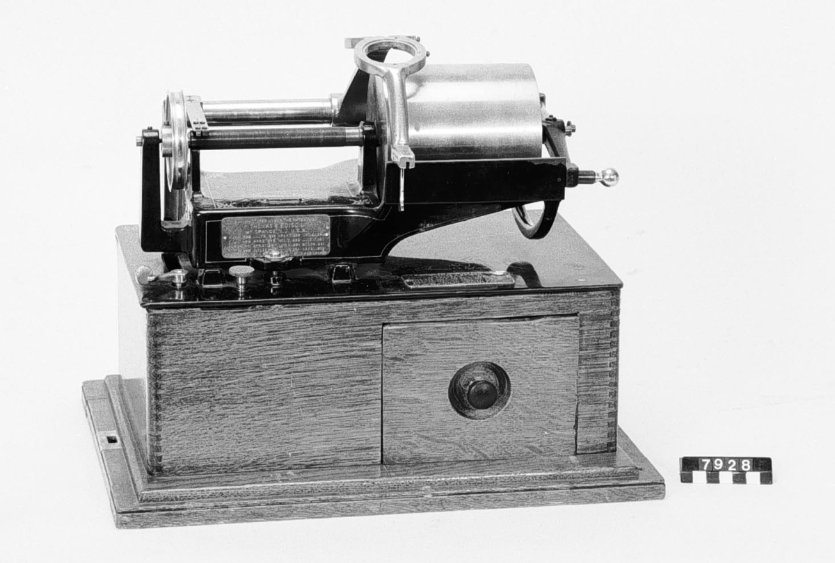 Fonograf, modell C, för "Grand" rullar enligt Edison, större typ med 2 synkroniserande ljuddosor och stora ljudtrattar av mässing. Märkt: Thomas A Edison. Orange Co. NJ.
Tillbehör: 23 st. vaxrullar (vilka saknas) för återgivning av musik (12 st. hela, 11 st. skadade) packade i 2 korgväskor, 2 st. ljudtrattar i fodral, 2 st. ljuddosor (extra), 2 gummislangar (bytta) samt 1 vev. Flätad konisk korg med lock (trattarna skall skjutas in i varandra).