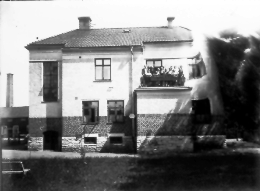 Baksidan av Skaraborgsbankens hus. På balkongen samma personer som på bild 28-6. Gamla mejeriets skorten i bakgrunden. (bilden skadad i kanten)