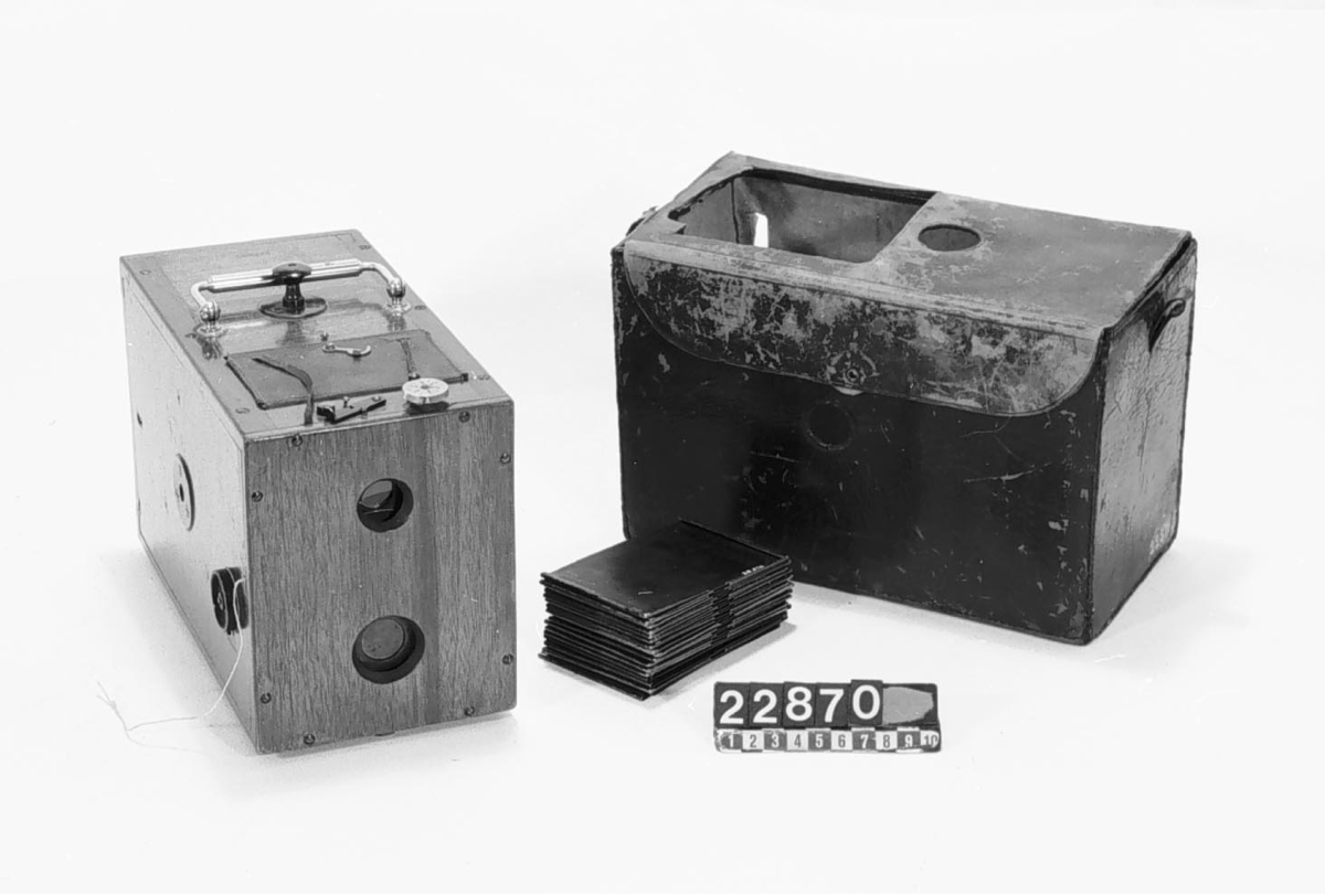 Lådkamera av trä, för plåtar 6.5 x 10 cm, i fodral av läder, med invändig plåtväxling. S.k. fallplåtskamera. Originell plåtväxling (troligen patent). Stor brilljantsökare med uppfällbart bländskydd, roterande skivbländare, skilda knappar för tids- och momentexponering samt plåträknare. Ögonblicksslutare. 30 st metallplåtar
Tillbehör: Kamera, fodral av läder samt 30 plåthållare av svart bleckplåt.
