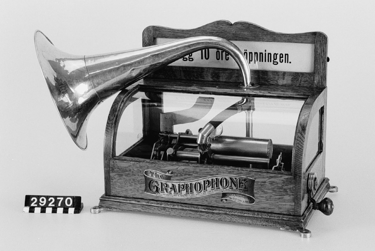 Fjäderdriven fonograf med fast vev, med automatisk spelning för en kostnad av 10 öre. Skyltens höjd: 115 mm.