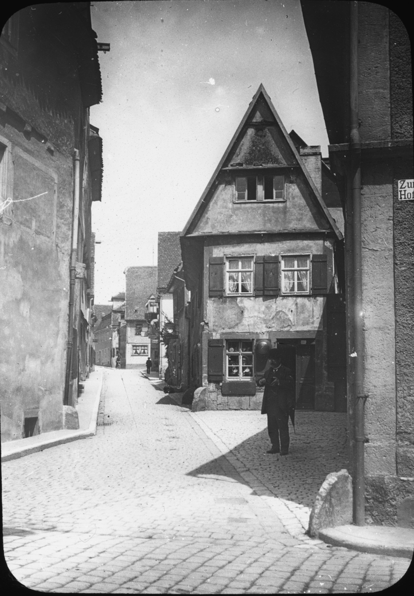 Skioptikonbild med motiv av man på gata/ gränd i Rothenburg.
Bilden har förvarats i kartong märkt: Vårresan 1910. Rothenburg XXIX.