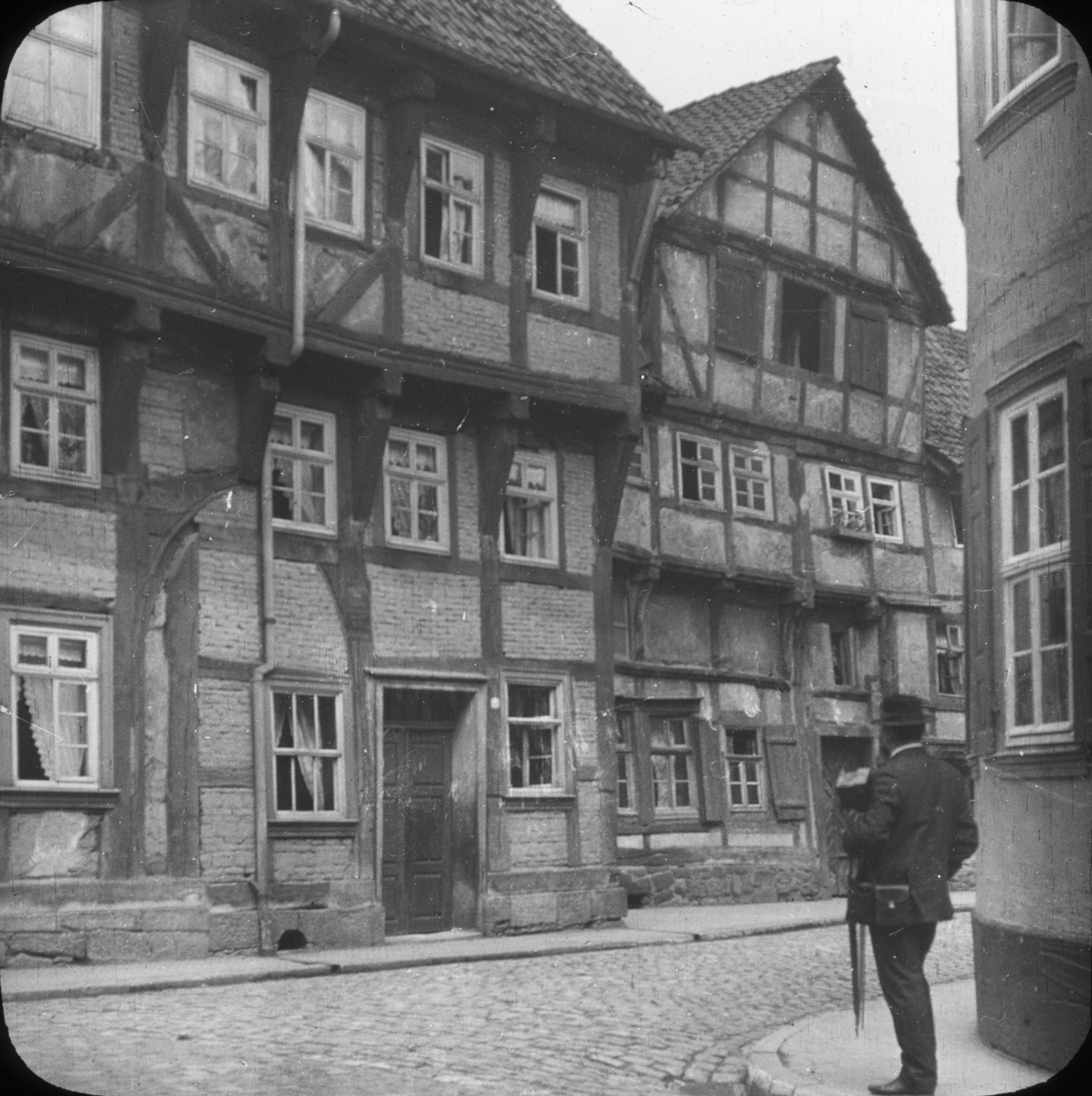 Skioptikonbild med motiv av man som betraktar ett äldre hus, Hannoversch-Münden.
Bilden har förvarats i kartong märkt: Resan 1904. München
