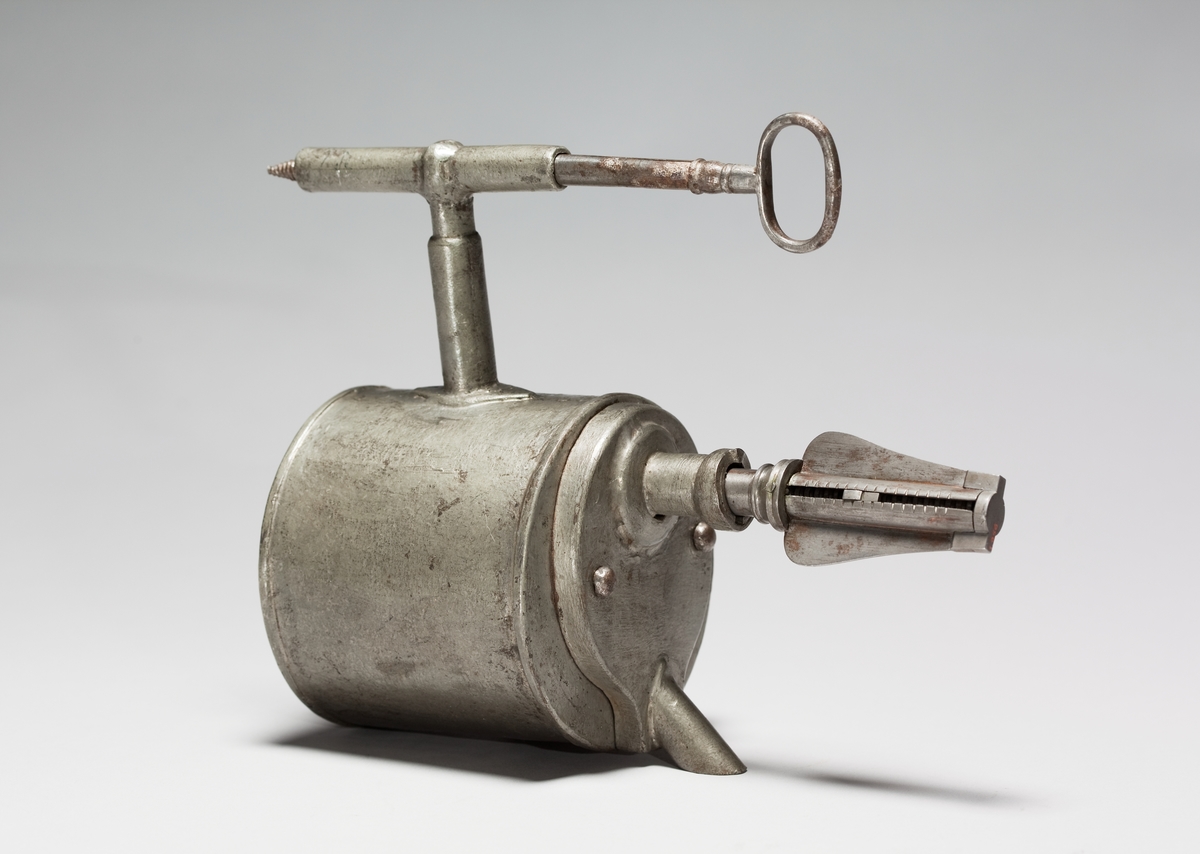 Christopher Polhem's strange tap, made of tinplate with the fixed parts riveted and soldered. The gear and its sleeve, the sleeve on the pipe and a liner in the drain of the container are made of brass. The tap is to be mounted in the barrel. The amount of liquid that is drawn out is portioned with a key. It also functioned as a lock and limited access to the barrel's contents. This specimen was probably exhibited at the 1866 exhibition in Stockholm, by "Stiernsunds Bruksegare", according to a contemporary exhibition catalogue.
