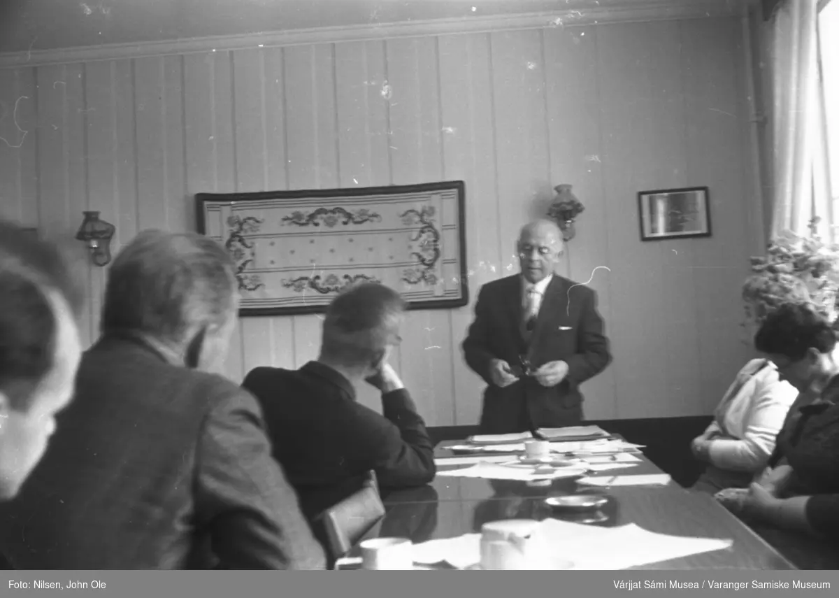 Seks personer samlet til et møte. Samme sted som på VSM.F.000809. Mannen med briller ved enden av bordet som holder hånden under haka er Karstein Evjen fra Vestre Jakobselv. Ukjent sted, 1966.