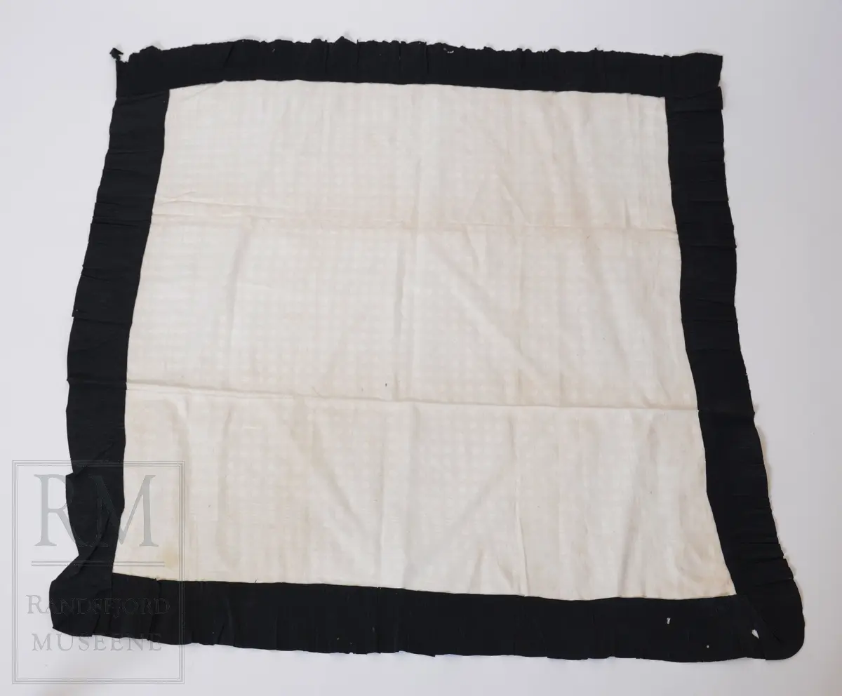 Kvadratisk duk i lin- dreiel med påsydd sørgekant av svart kreppapir (bånd)