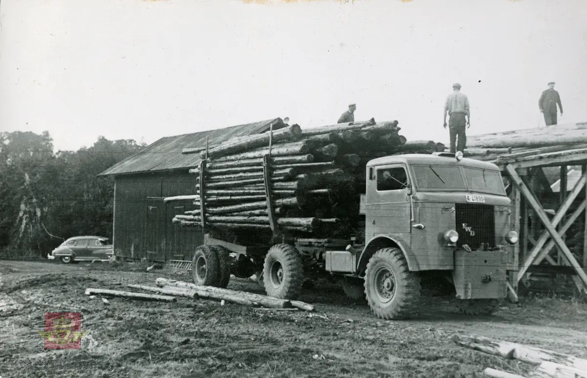 FWD lastebil, med kjennemerke A-41890, kjører tømmertransport. Sannsynligvis er det Colbjørnsen sin DeSoto med solskjerm på frontruten i bakgrunnen. Moderne tilbehør den gang. 1948.