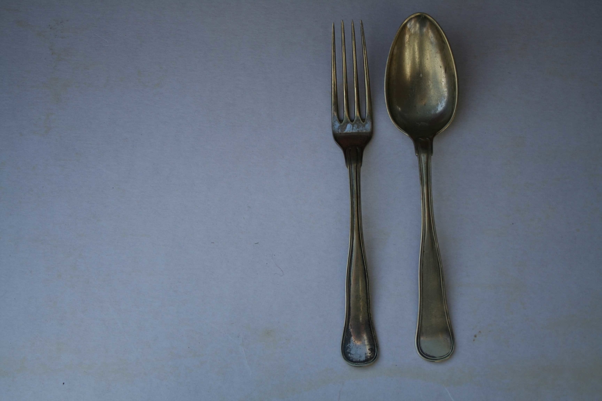 Skje og gaffel er heilstøpt i ei sølvlegering, utan spesielt mønster berre to opphøde liner i ytterkant i skaftet. 