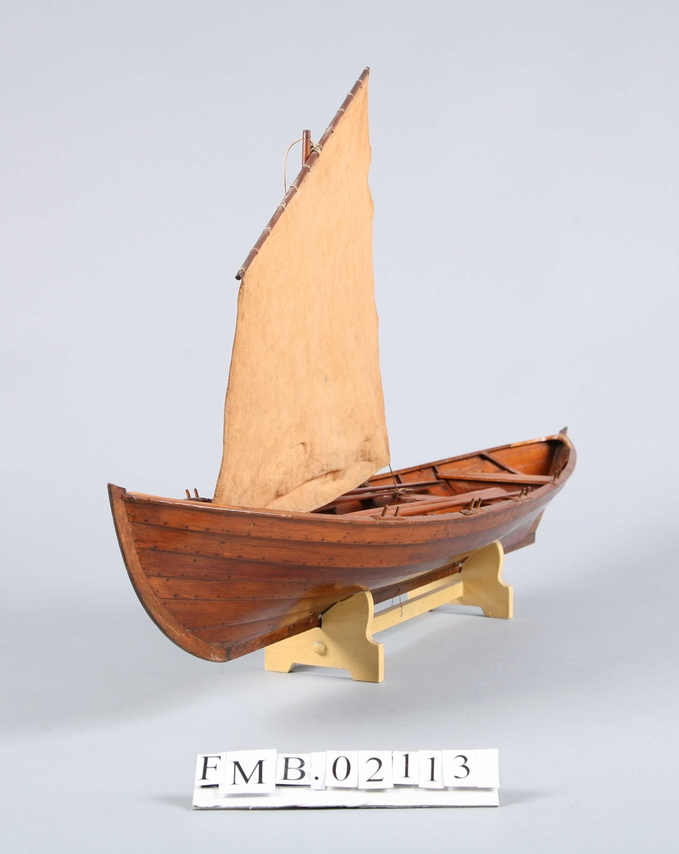 Sjekte med mast, seil og 4 årer. Den har 6 par tollepinner. Båtmodellen står på en støtte (krybbe).